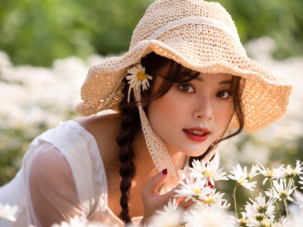 Девушка азиатка в шляпке на поле с ромашками