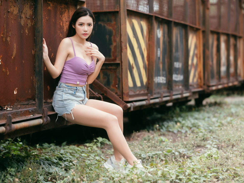 Девушка азиатка сидит у ржавого вагона