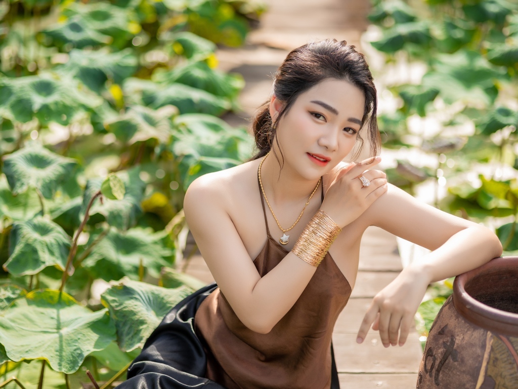 Девушка азиатка сидит у зеленых листьев лотоса