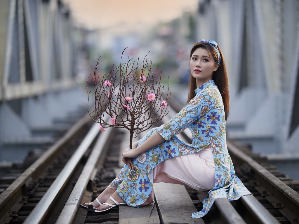 Девушка азиатка с деревом сидит на рельсах