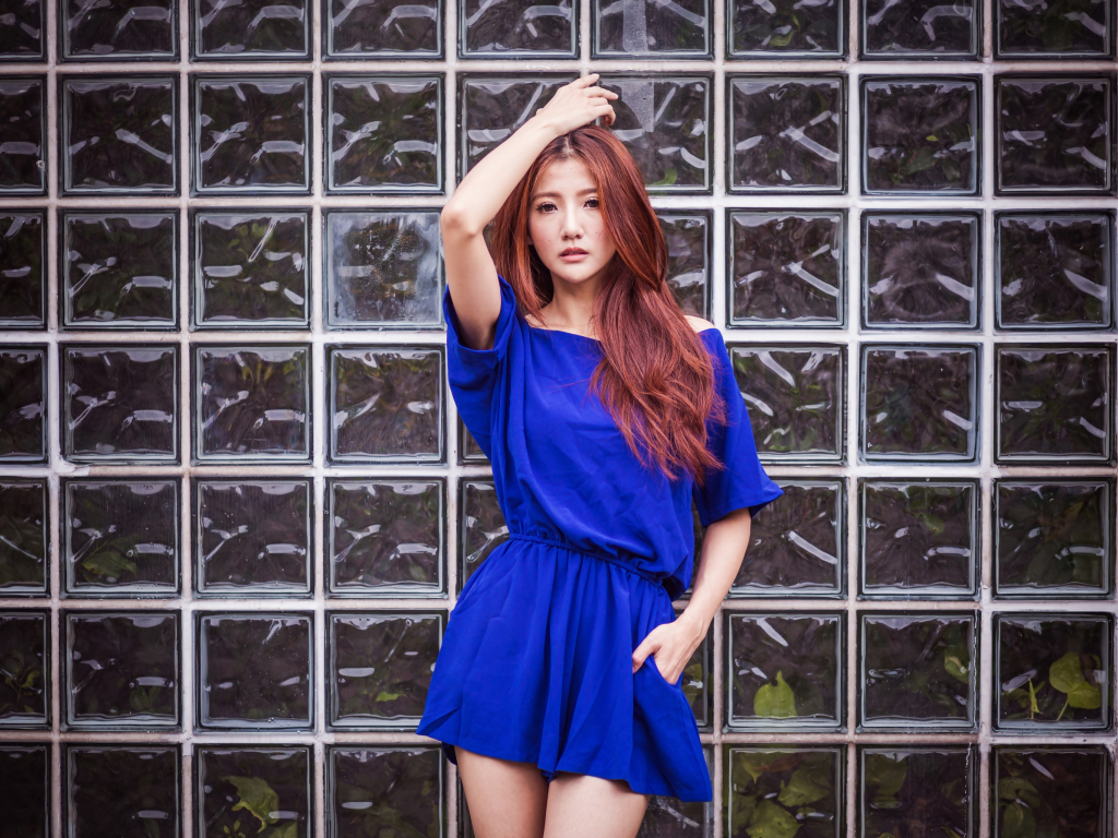 Азиатка в синем платье стоит у стеклянной стены