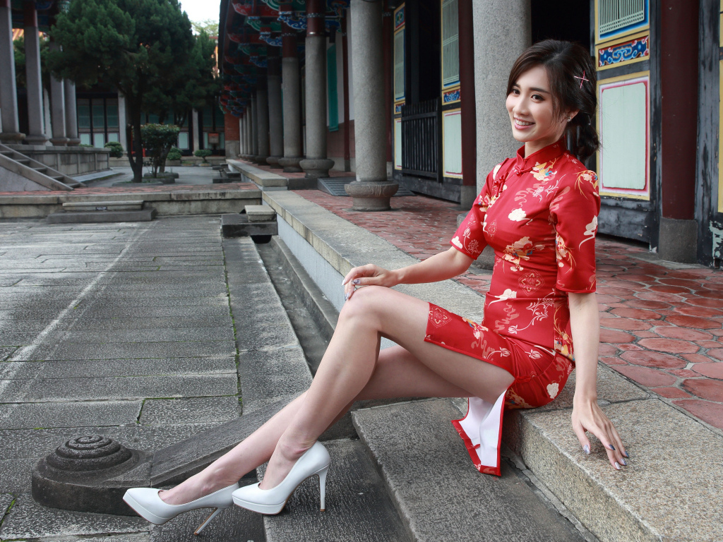 Улыбающаяся девушка азиатка в красном платье сидит на ступеньках