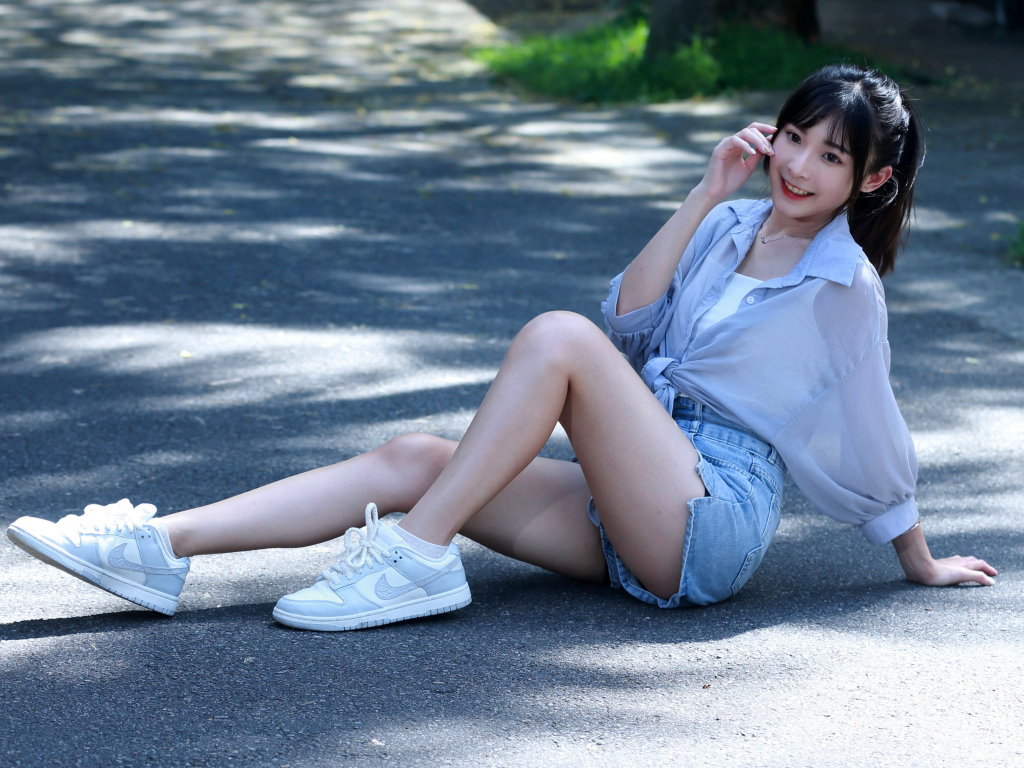 Улыбающаяся девушка азиатка в кедах сидит на дороге