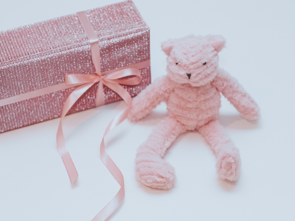 Подарок с розовой игрушкой на сером фоне