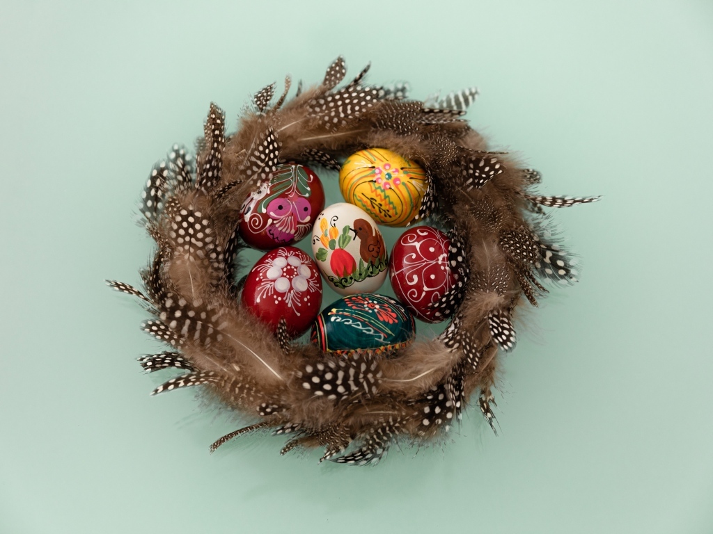 Красивые разноцветные яйца в гнезде из перьев на сером фоне