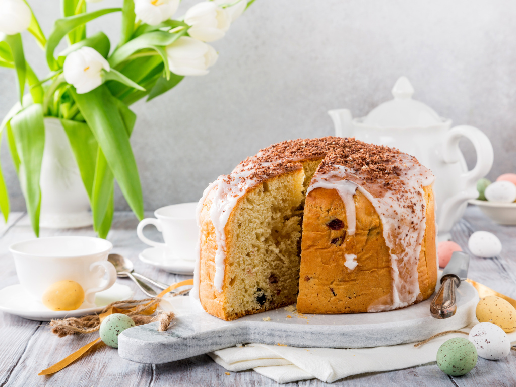 Пасхальный кулич на столе с букетом тюльпанов и сладостями