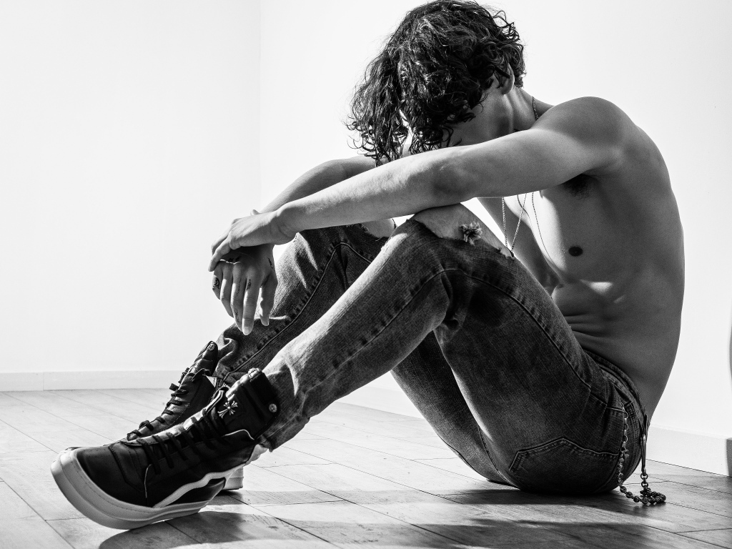 Грустный мужчина в джинсах сидит на полу