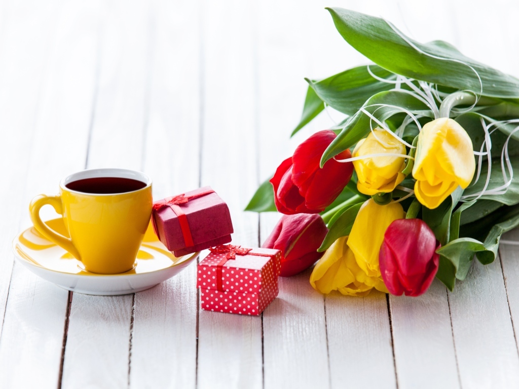 Желтая чашка кофе на столе с подарками и букетом тюльпанов