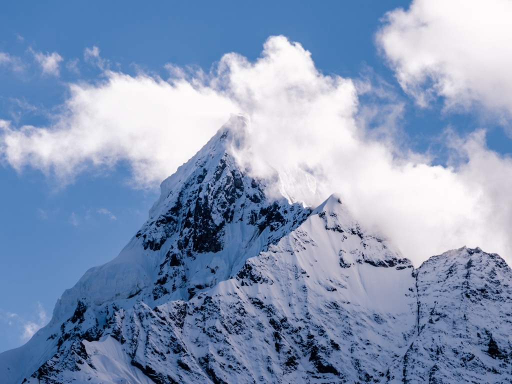 Острая заснеженная вершина горы в белых облаках