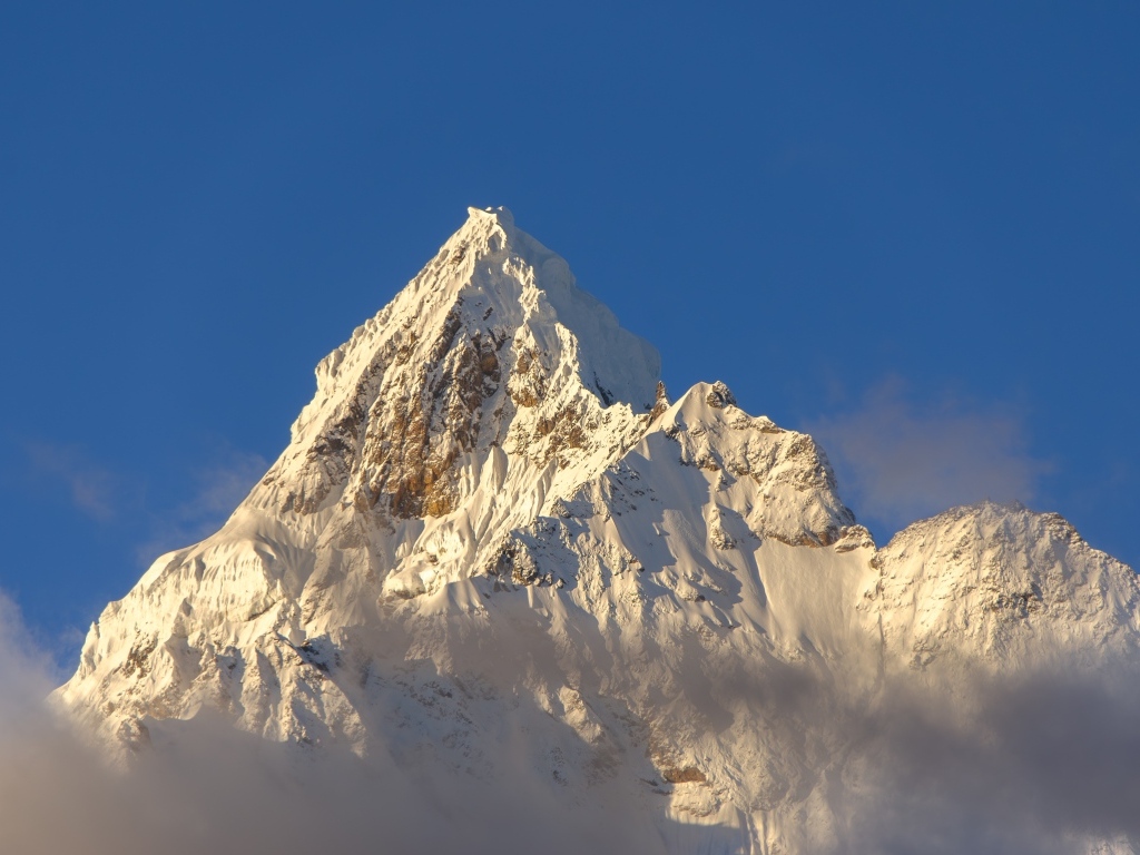 Крутая заснеженная вершина горы на голубом фоне