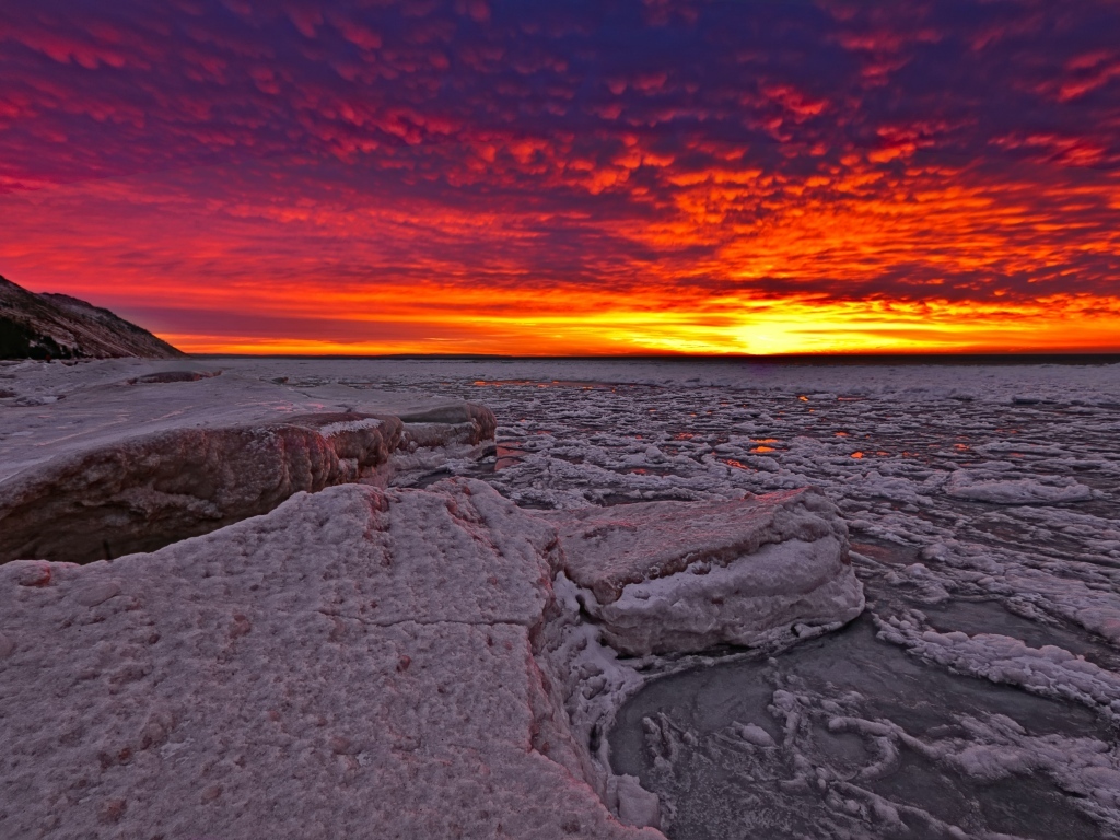 Красный закат солнца покрывает заледеневшее озеро 