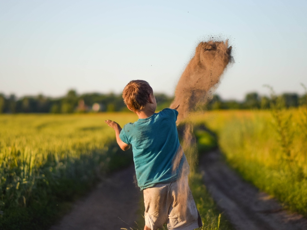 Мальчик бросает песок на дороге