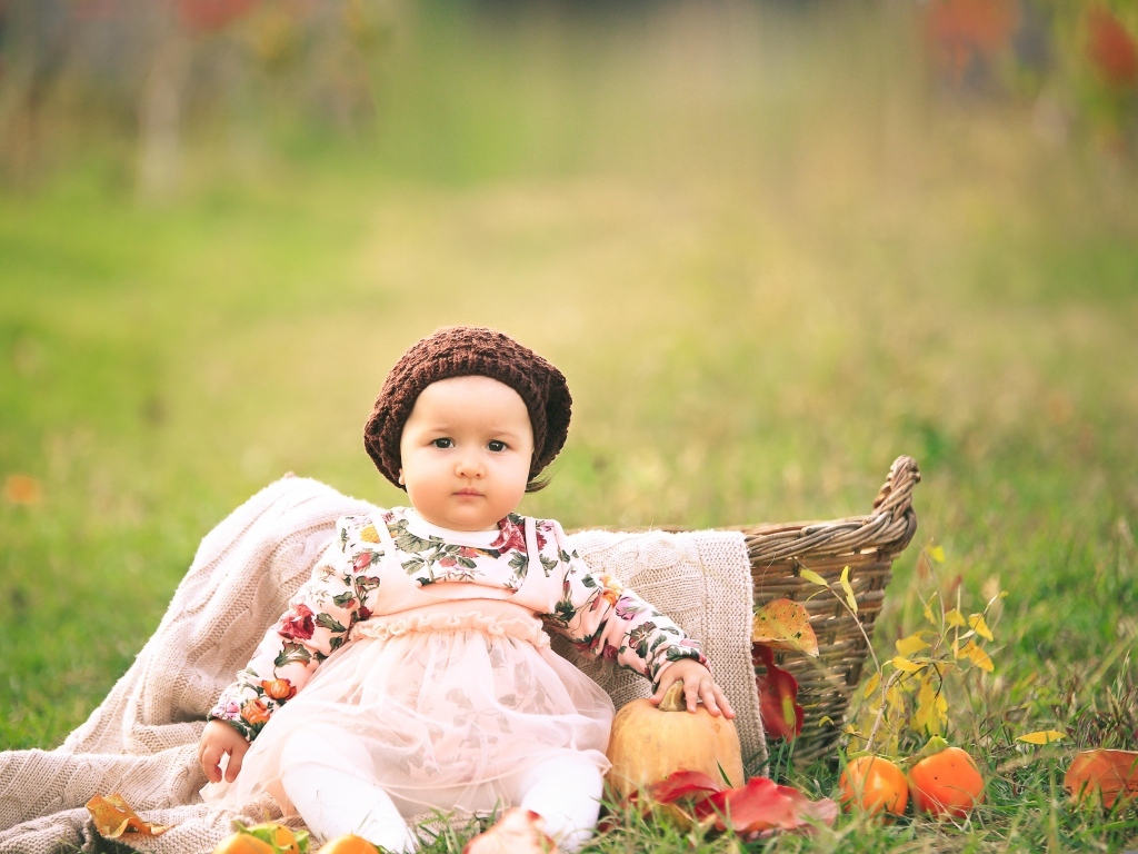 Милая маленькая девочка в шапке сидит на траве 