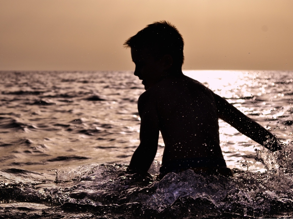 Маленький мальчик купается в воде летом