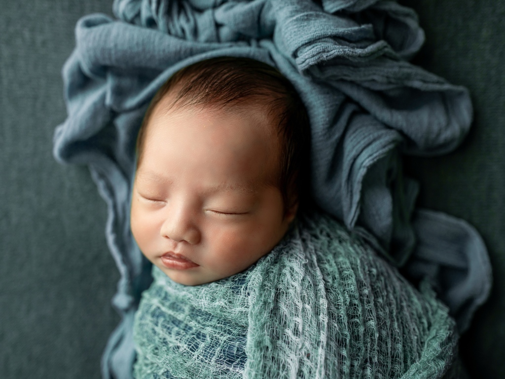 Новорожденный ребенок завернут в серое покрывало 