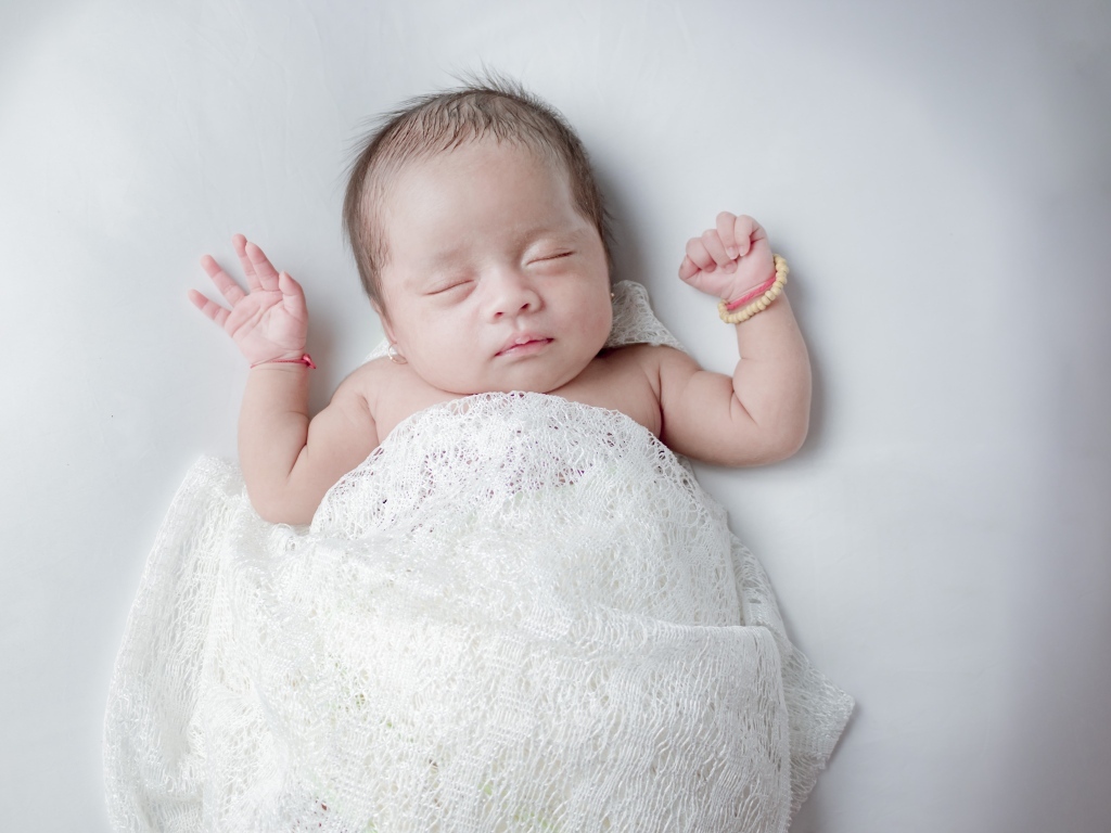 Маленький спящий ребенок на сером фоне под белым покрывалом