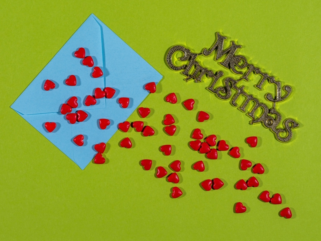 Красные сердечки и голубой конверт на зеленом фоне на Рождество