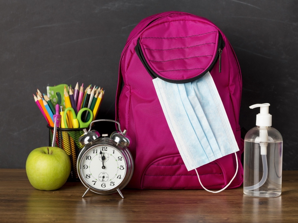 Рюкзак на столе с будильником, ручками и яблоком