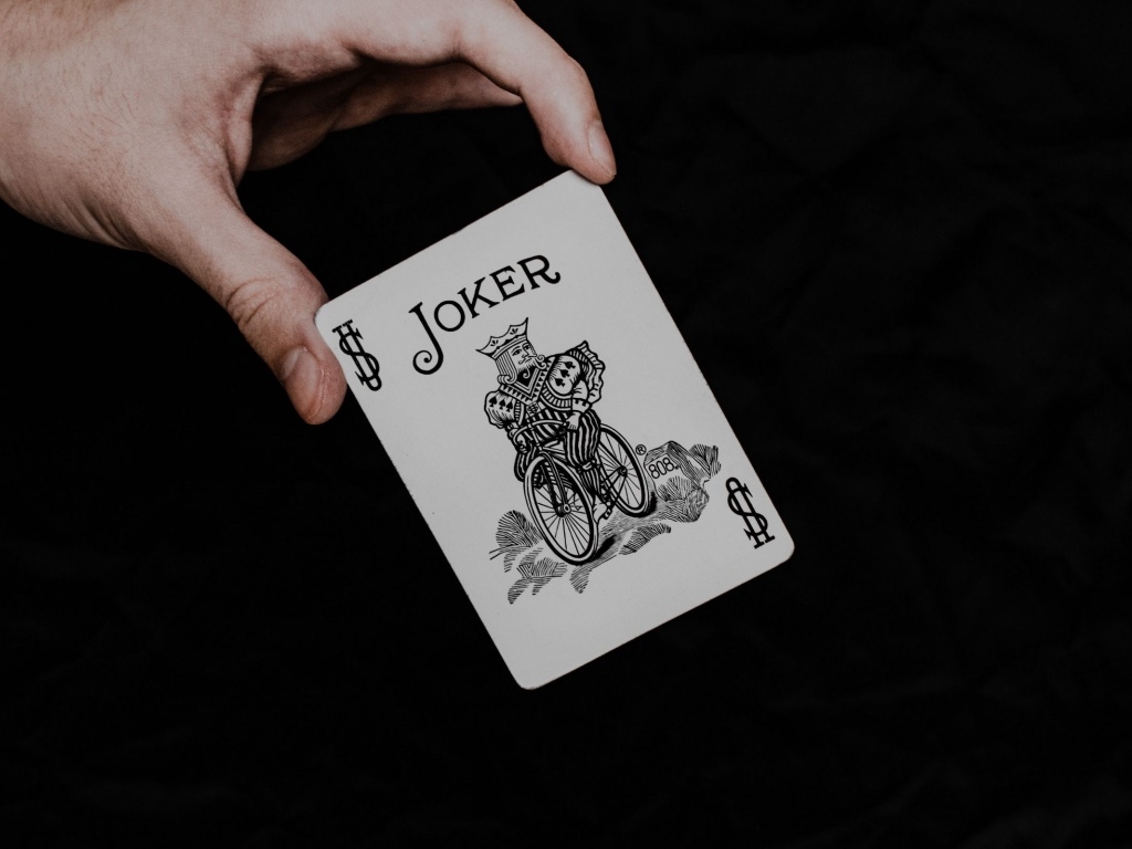 Карта Джокер в руке на черном фоне