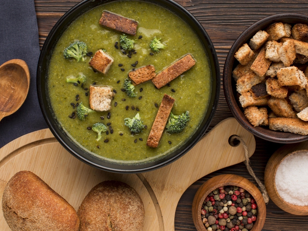 Зеленый суп пюре на столе с сухариками и перцем