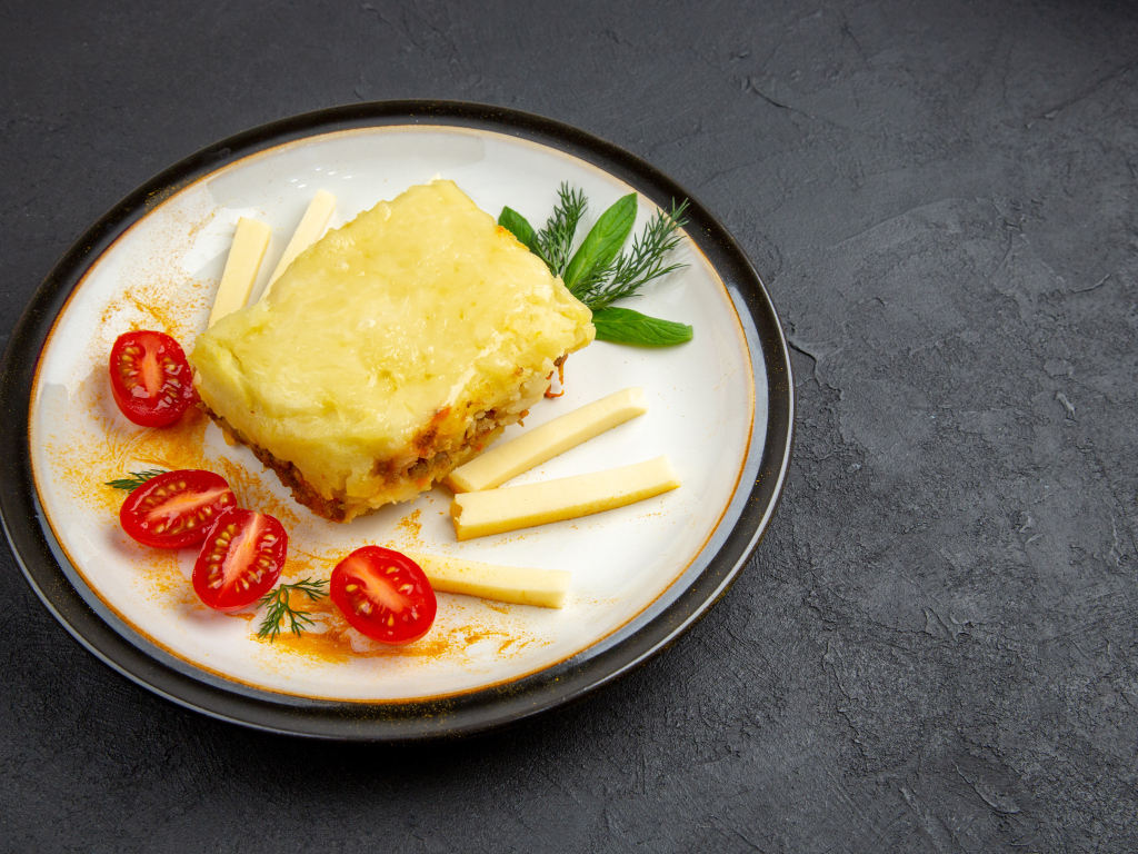 Кусок картофельной запеканки на тарелке с помидорами