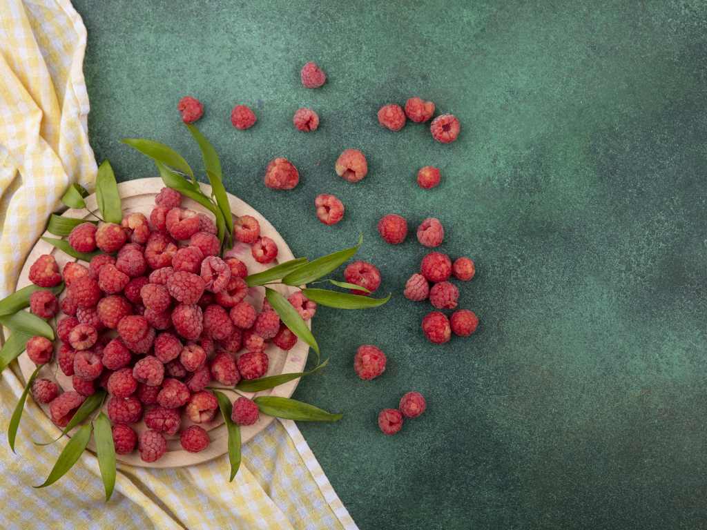 Красная малина с зеленой листвой на столе