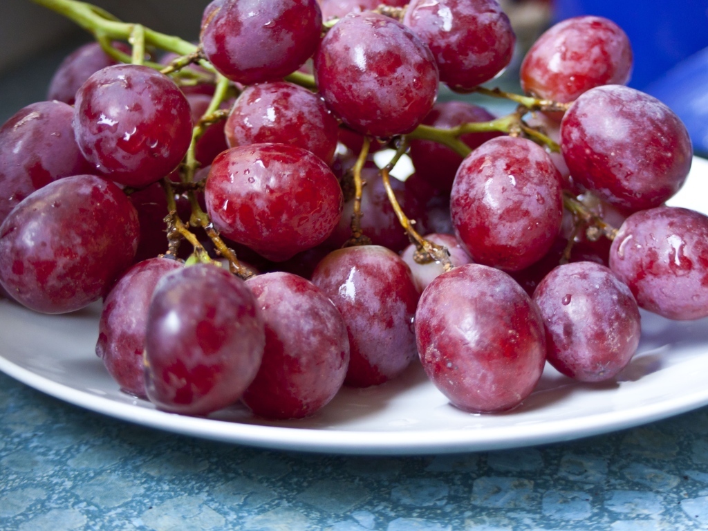 Спелый розовый виноград на белой тарелке