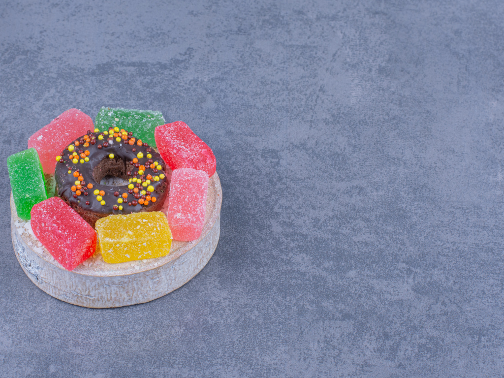 Разноцветные мармеладные конфеты и пончик на сером столе