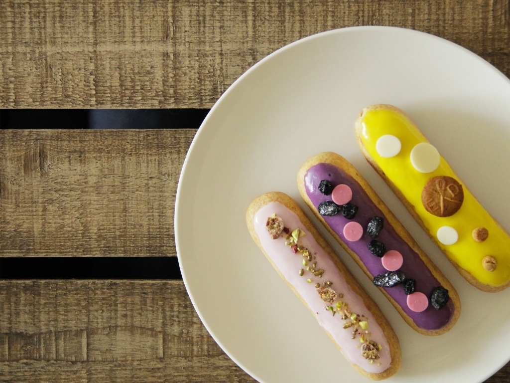 Три эклера на белой тарелке на деревянном столе