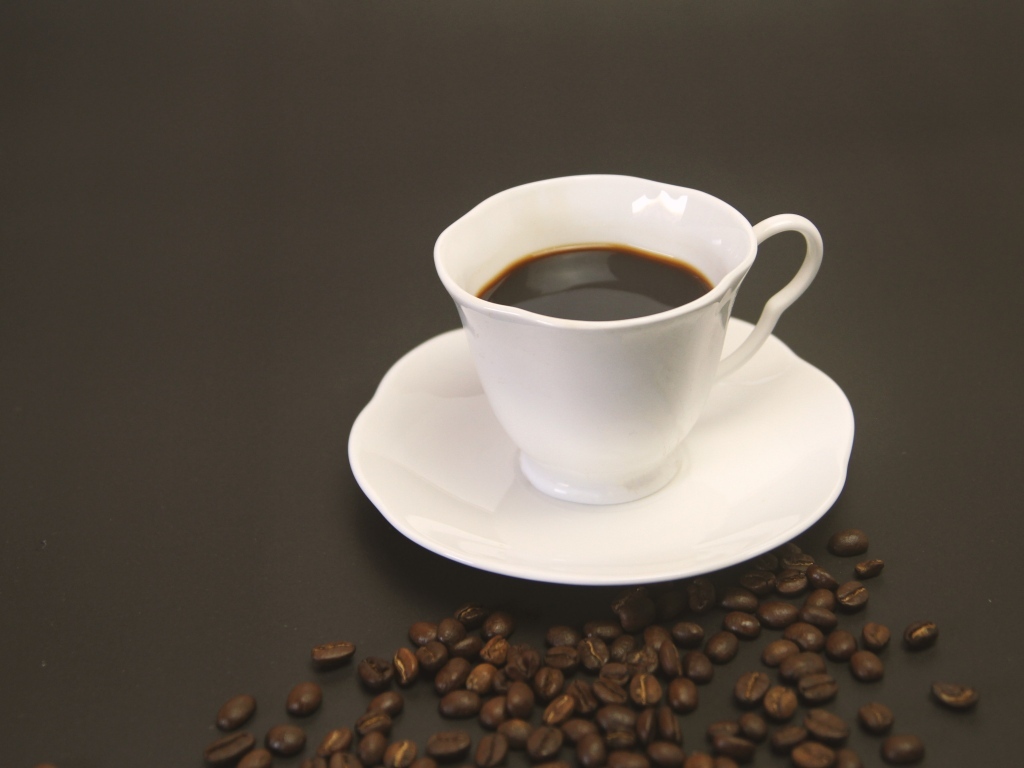 Белая чашка с кофе на столе с зернами