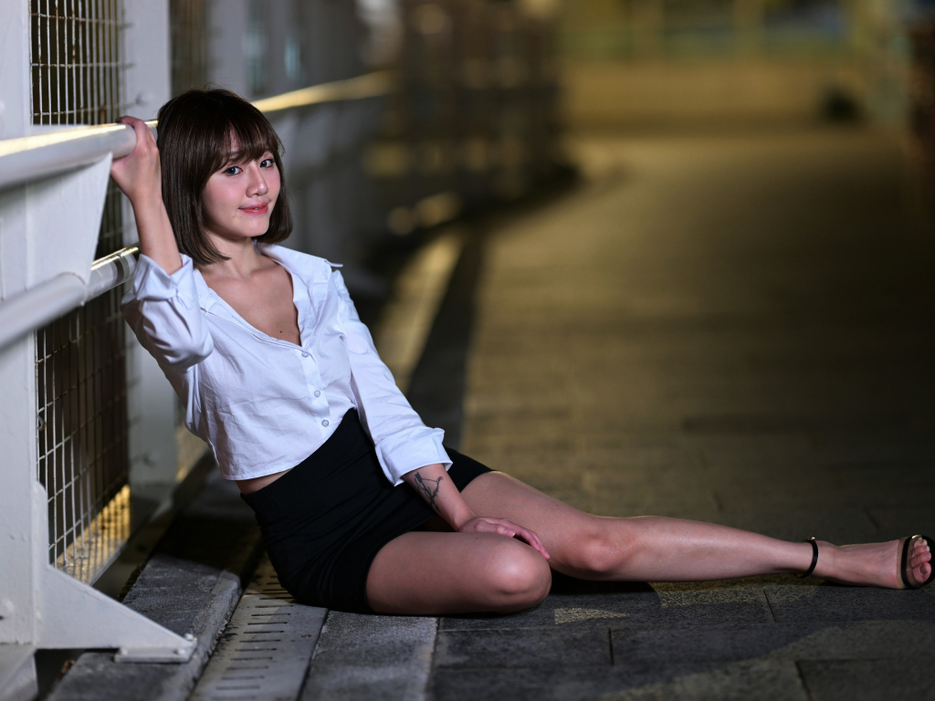 Девушка в черной юбке и белой рубашке сидит на дороге