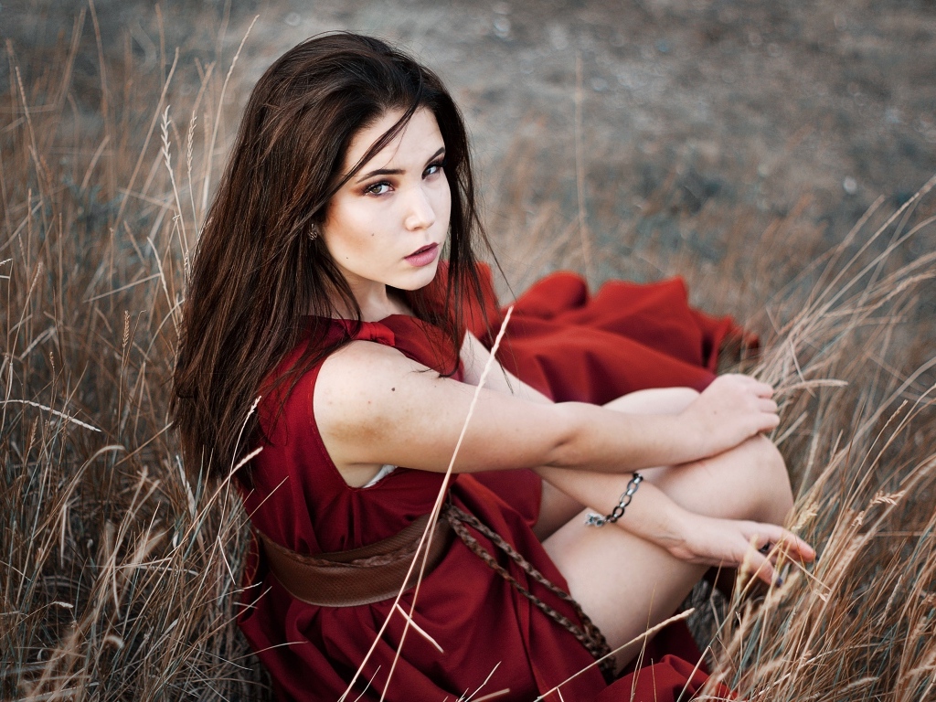 Девушка в красном платье сидит в траве