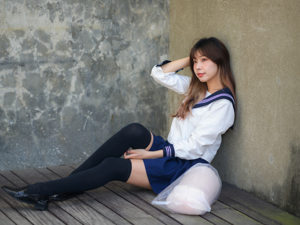 Азиатка в черных чулках сидит у стены