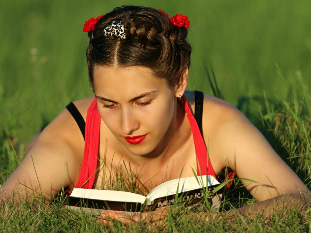 Красивая девушка читает книгу лежа на траве
