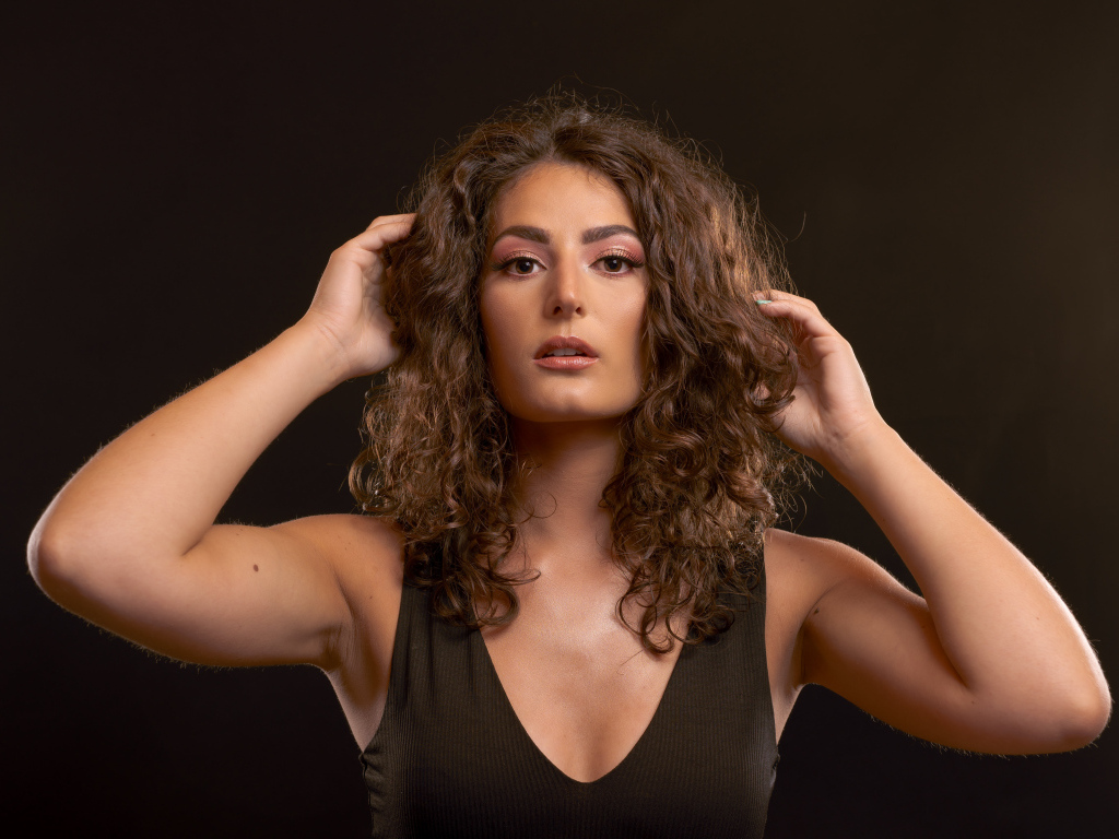 Кудрявая девушка держит руки в волосах на черном фоне