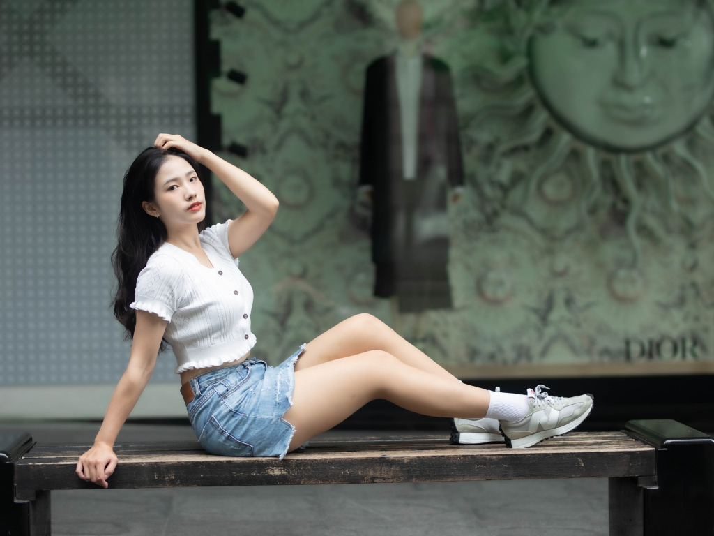 Милая девушка азиатка в белой кофте лежит на лавке