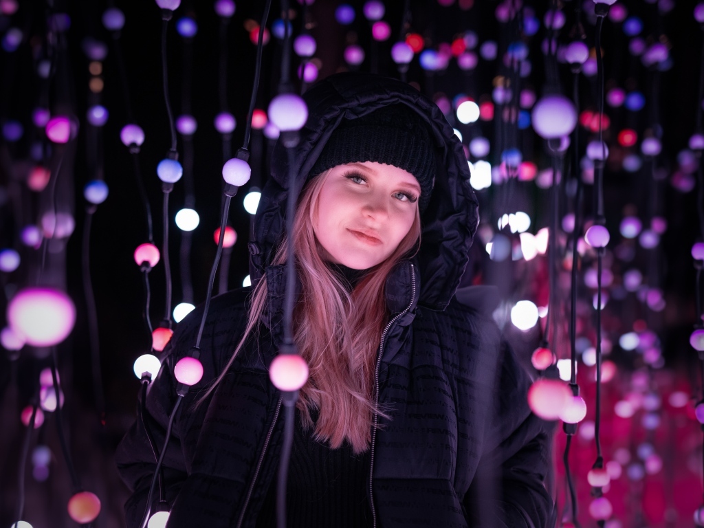 Девушка в черной куртке у светящейся гирлянды