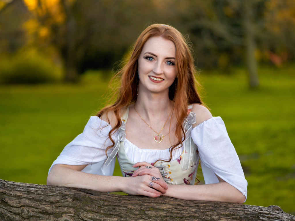 Улыбающаяся рыжеволосая девушка стоит у дерева