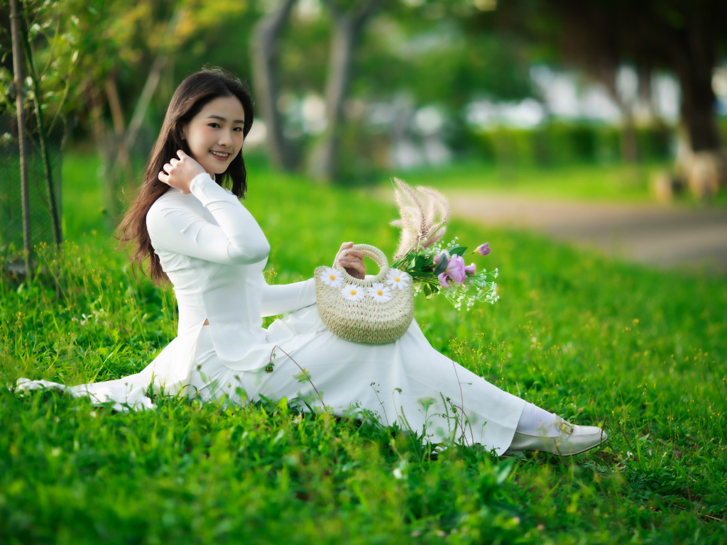 Нежная азиатка в белом наряде сидит на траве