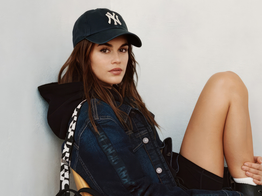 Красивая модель Кайя Гербер в кепке сидит у стены