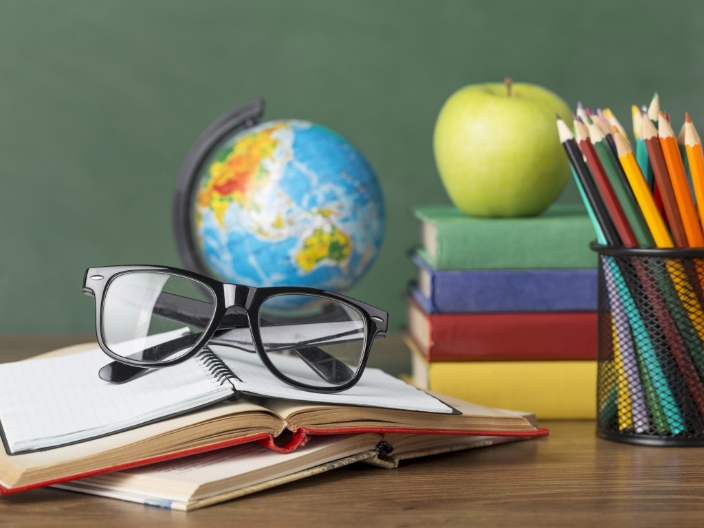 Книги, очки и карандаши с глобусом на столе у доски
