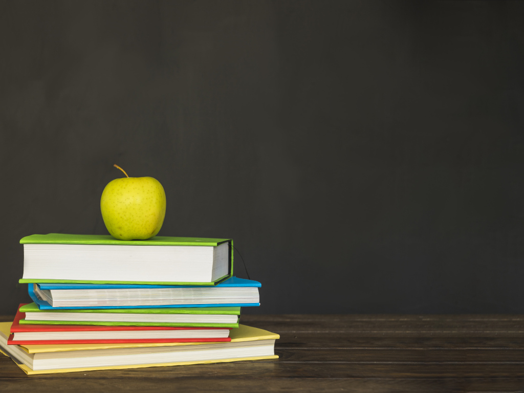 Разноцветные книги с зеленым яблоком на фоне доски