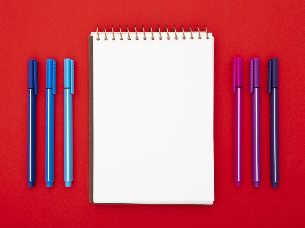 Блокнот и фломастеры на красном фоне