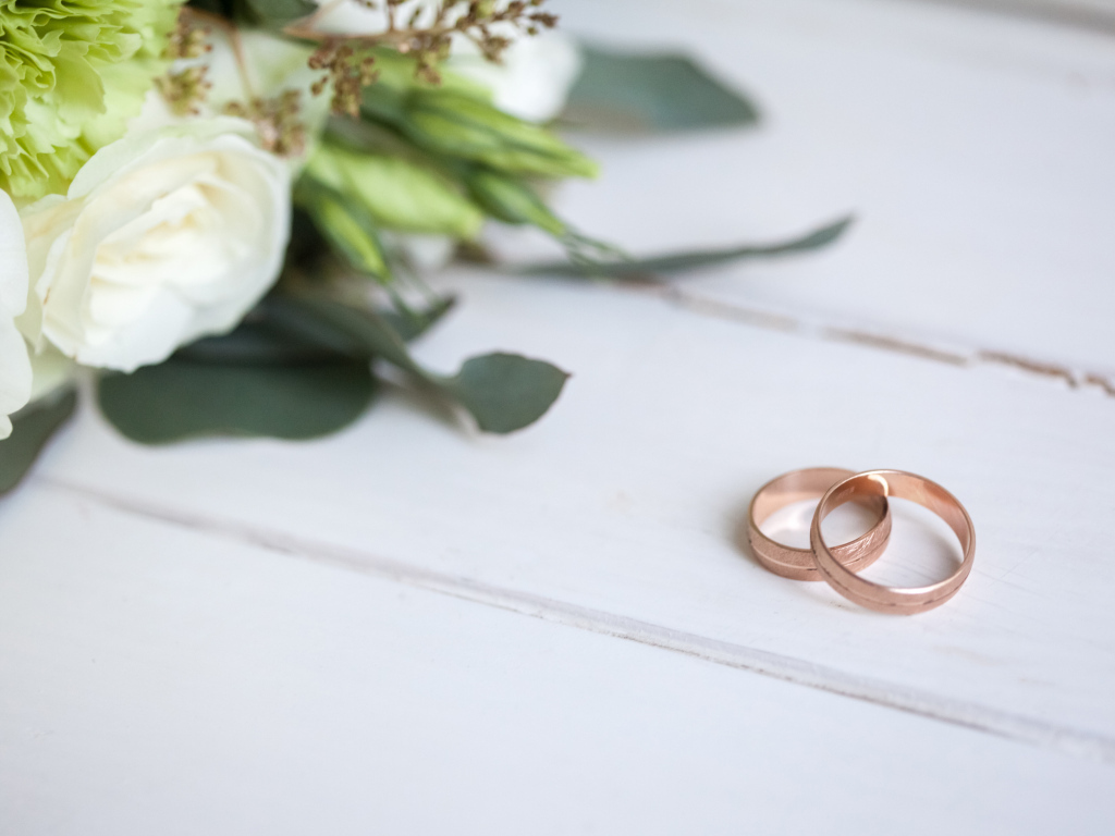 Два золотых обручальных кольца с букетом на белом столе