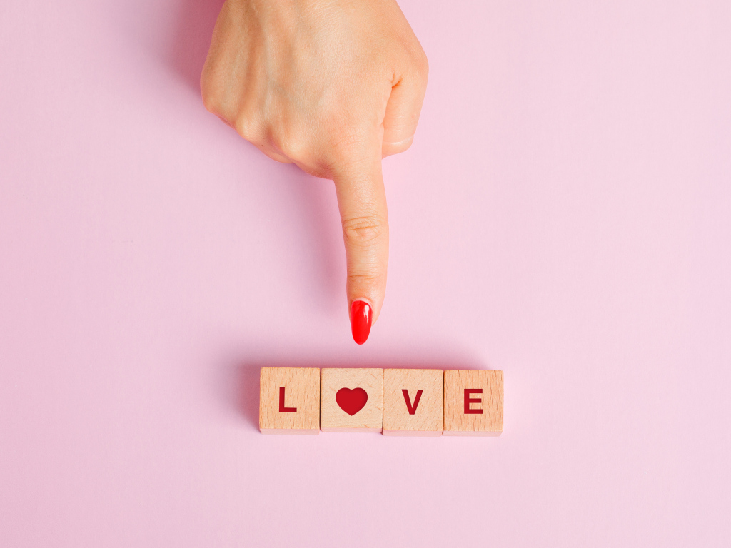 Рука указывает на кубики с надписью любовь на розовом фоне