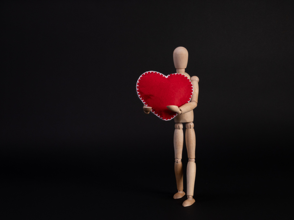 Марионетка держит красное сердце на черном фоне