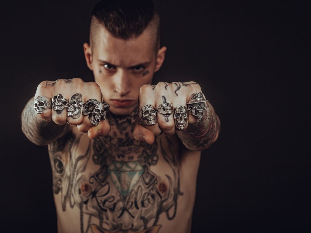 Мужчина с татуировками на теле показывает перстни на пальцах