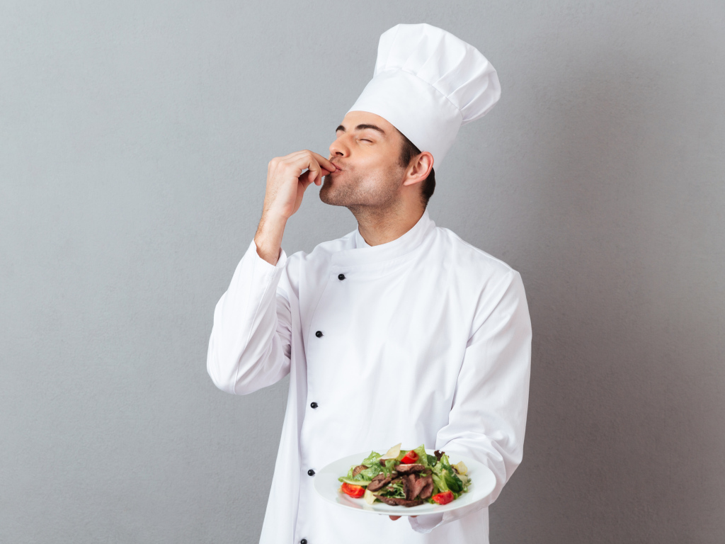 Мужчина повар в белом костюме с блюдом на сером фоне