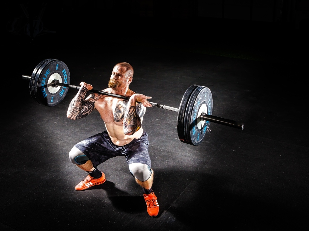 Сильный мужчина с татуировками на теле поднимает штангу