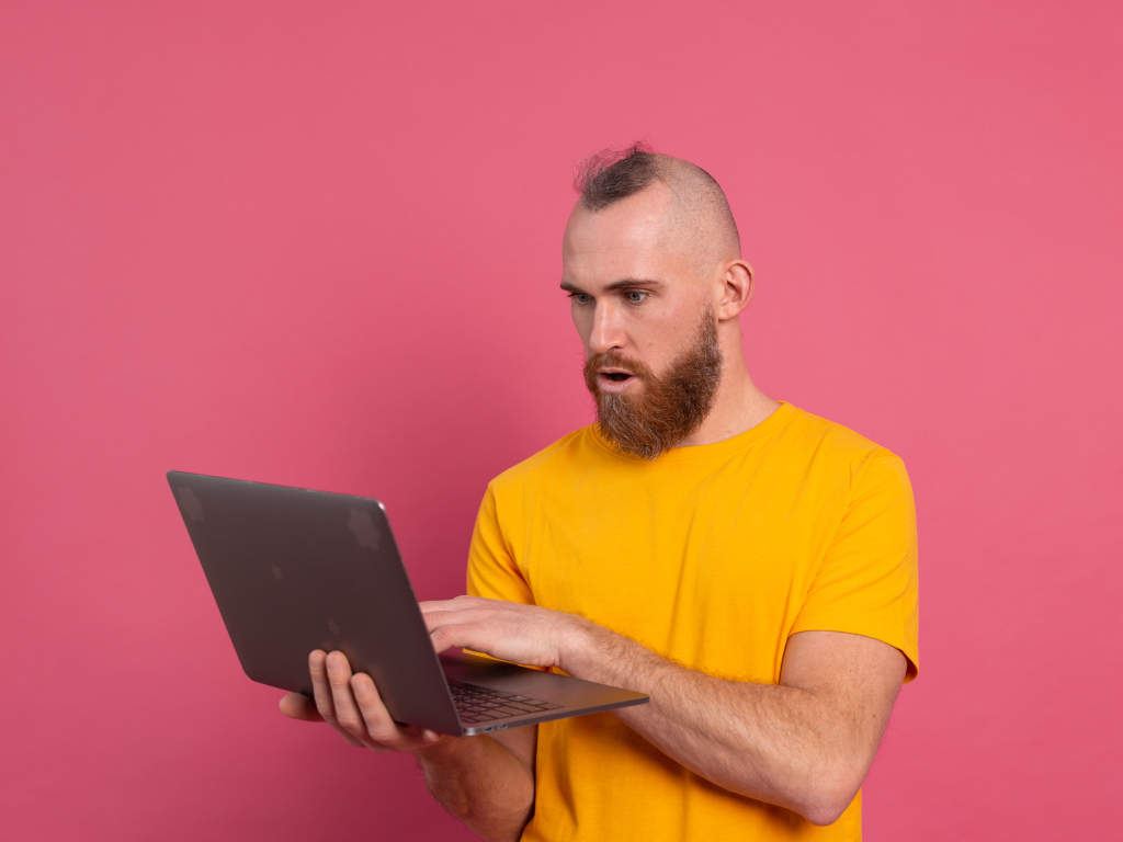 Удивленный мужчина с ноутбуком на розовом фоне